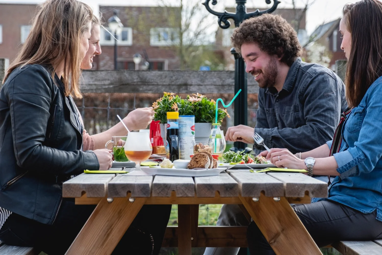 Drie gasten praten en drinken aan een picknicktafel op het terras