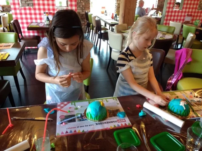 Twee meisjes versieren hun eigen boltaart aan tafel tijdens een kinderfeestje