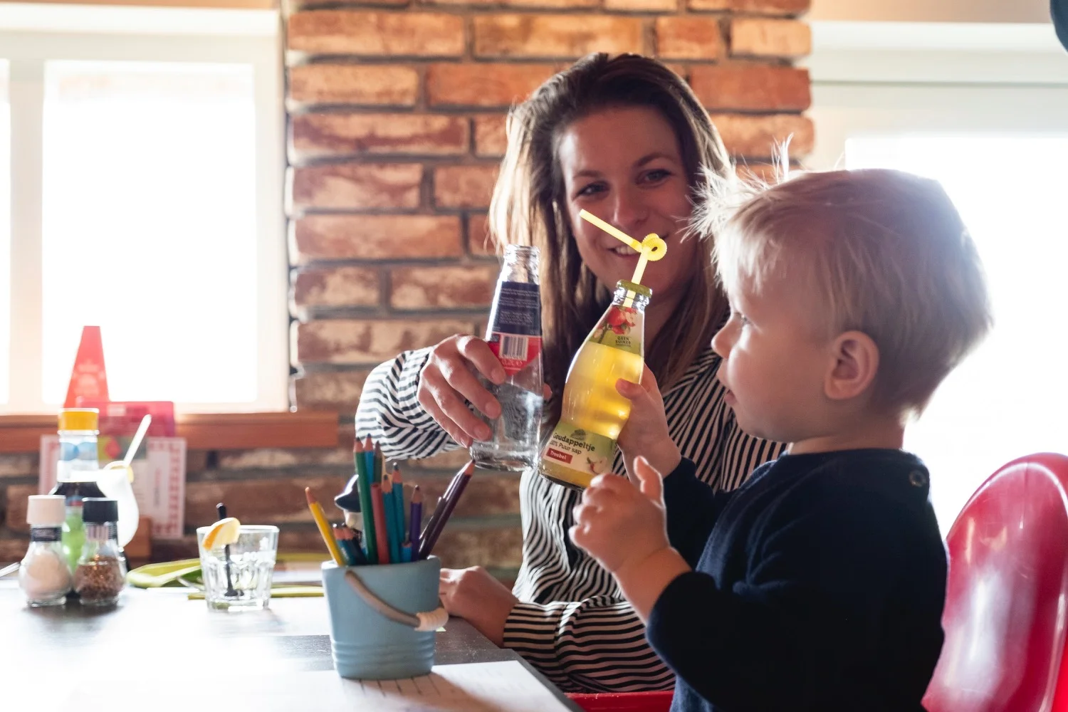 Moeder en peuter drinken samen uit een flesje aan tafel