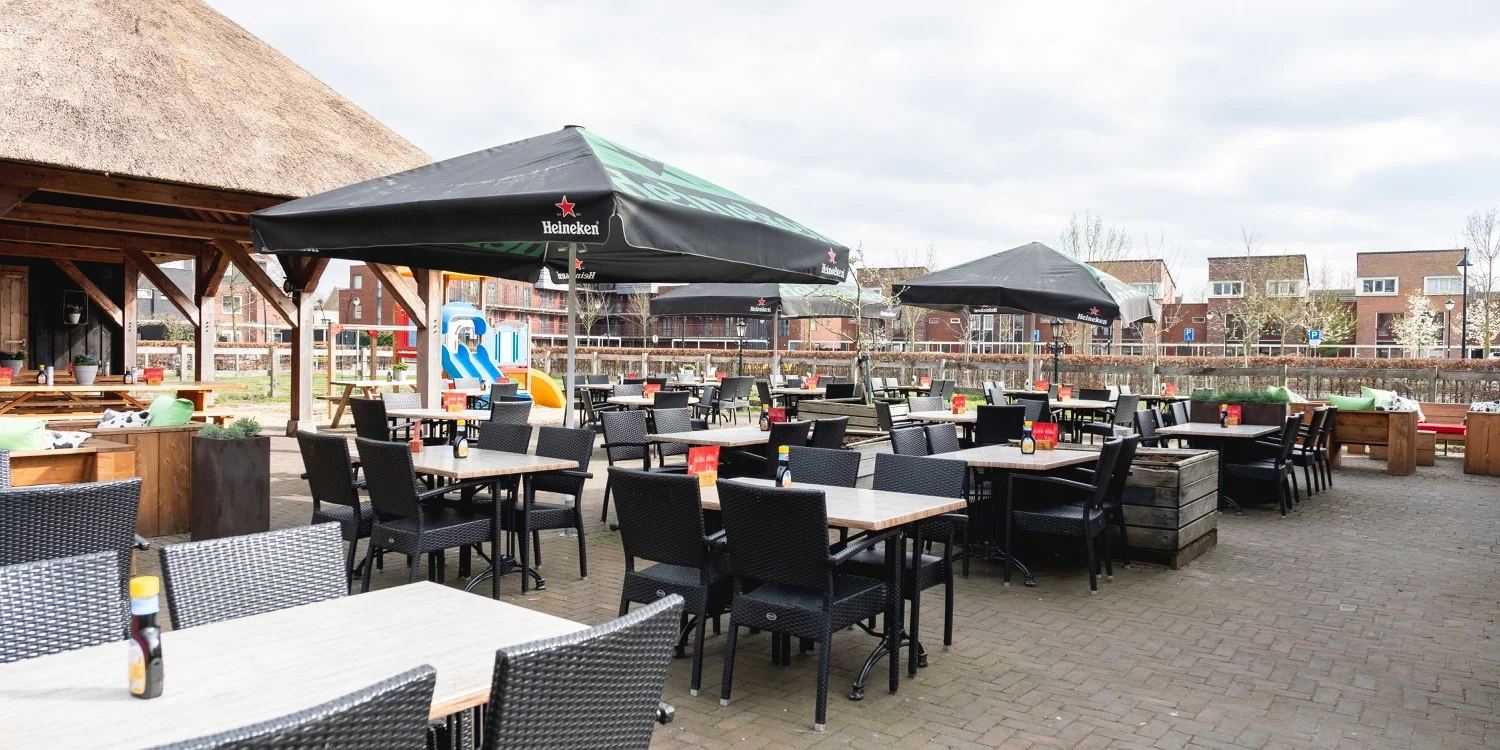 Overdekt terras met tafels en parasols, uitkijkend over de wijk
