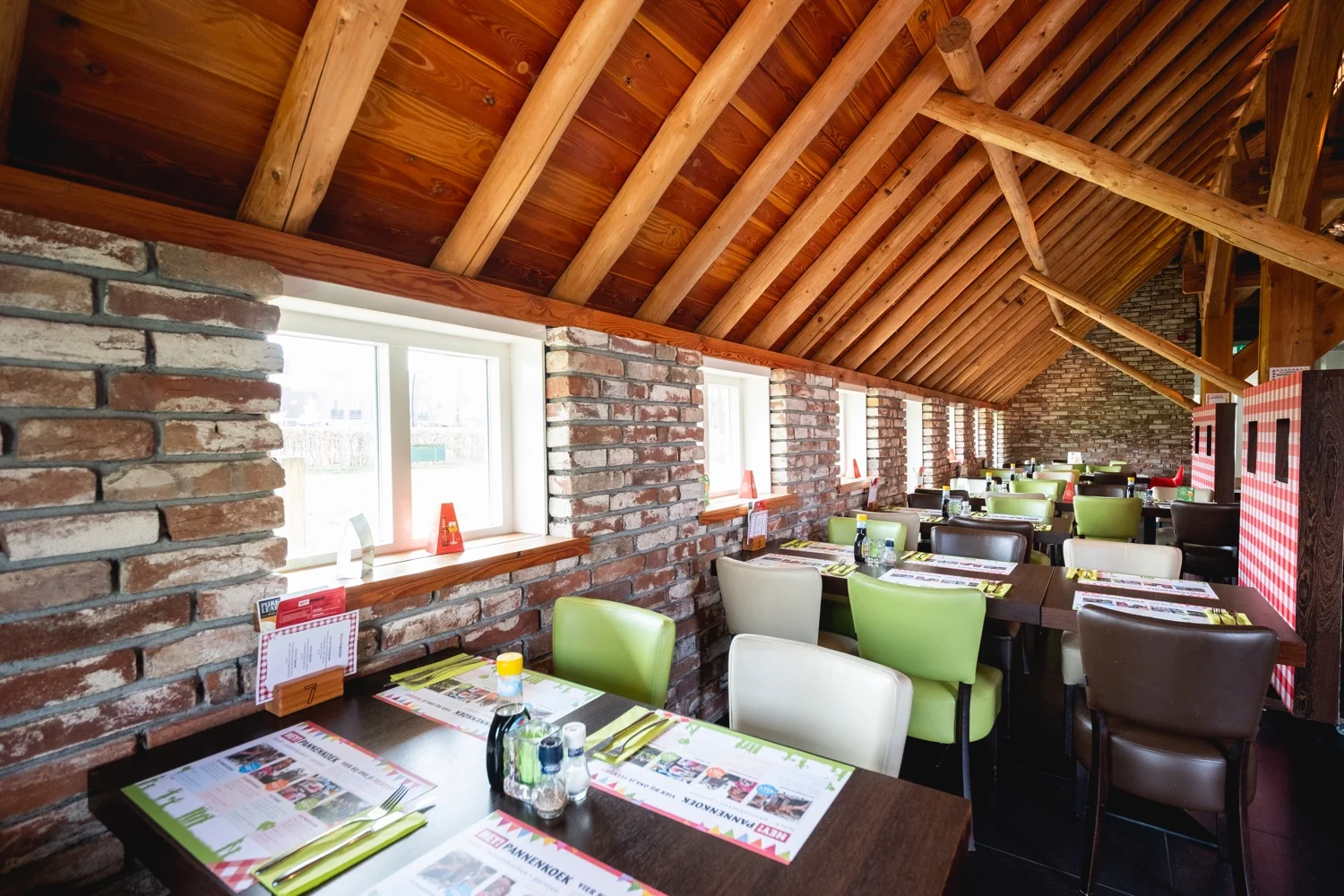 Restaurantzaal met bakstenen muur, houten spanten en gedekte tafels