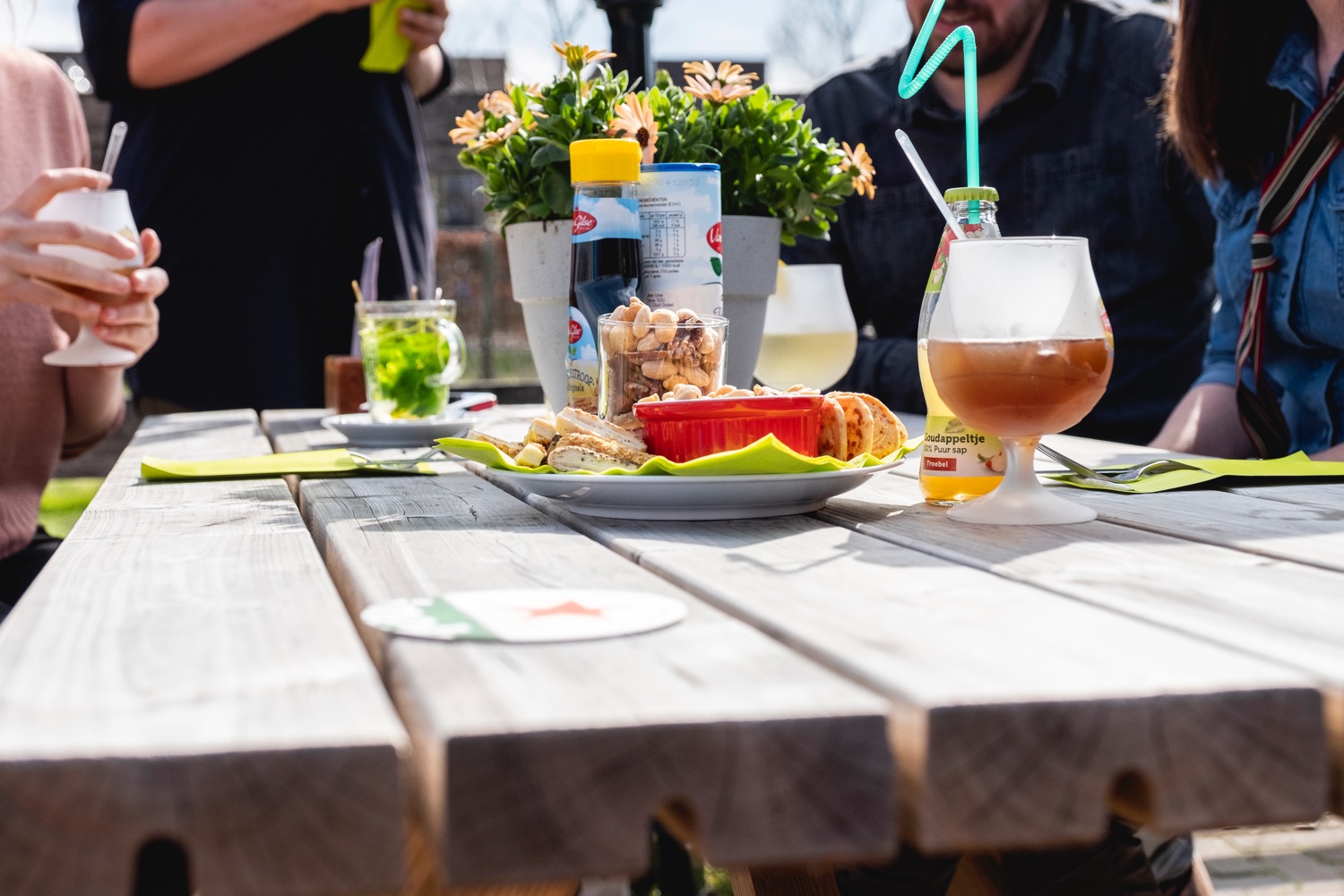Houten tafel buiten met drankjes, bloemen en een bord eten