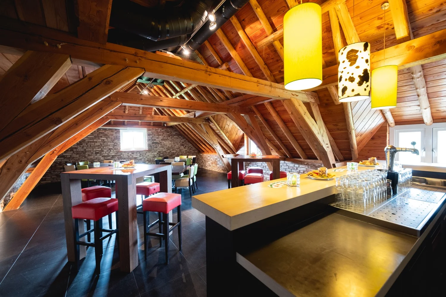Zaal met bar, rode krukken en houten spanten onder warm licht